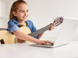 Cheerful girl with guitar using laptop