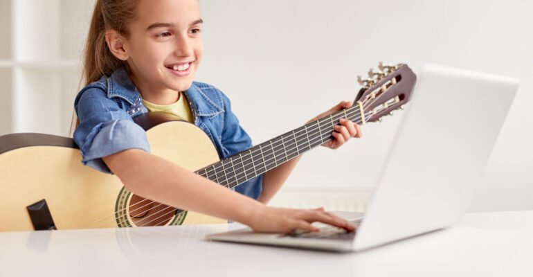Cheerful girl with guitar using laptop